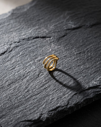 Stainless steel wave stack ring resting on a worn grey slate stone with natural light casting defined shadows.