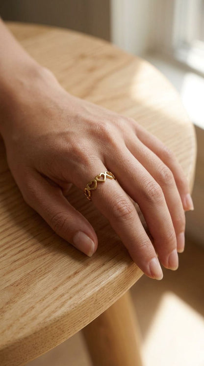 Full hand shot showcasing the tiny stainless steel heart ring on a relaxed woman's finger against a textured wooden surface.