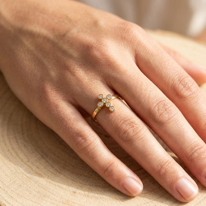 Woman's hand resting on wood showcasing the small gold-plated cross ring with rhinestones, emphasizing its delicate size and sparkle.