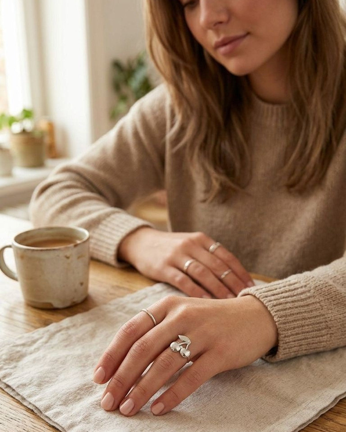 Full-body shot of woman wearing the Cherry Pop Statement ring, with her hand resting on a textured surface in a warm, casual indoor setting.