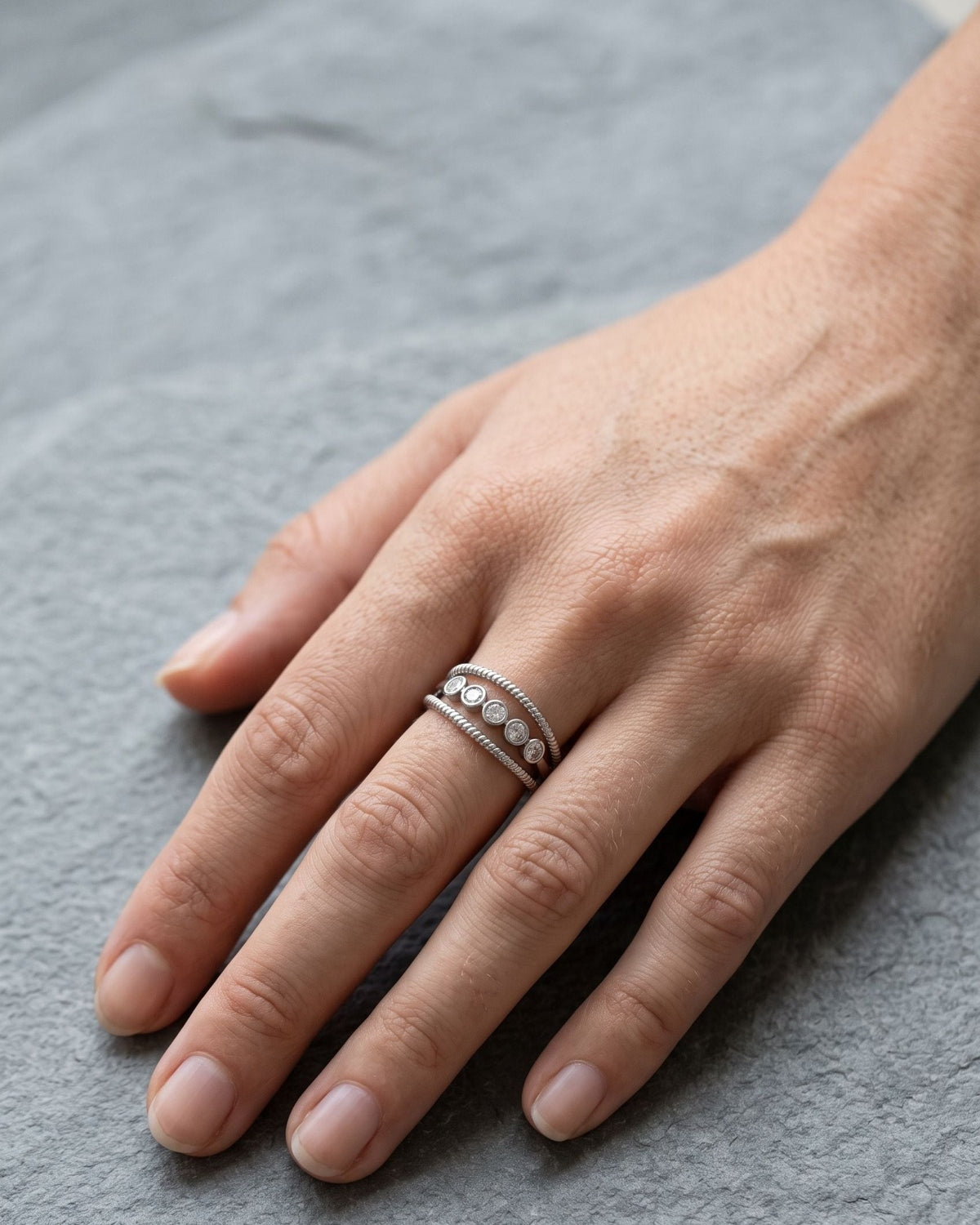 Woman wearing a dainty adjustable silver rhinestone ring on her hand while resting on a grey slate stone.