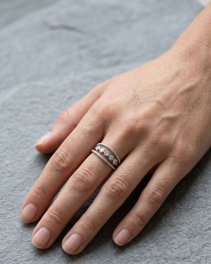 Woman wearing a dainty adjustable silver rhinestone ring on her hand while resting on a grey slate stone.