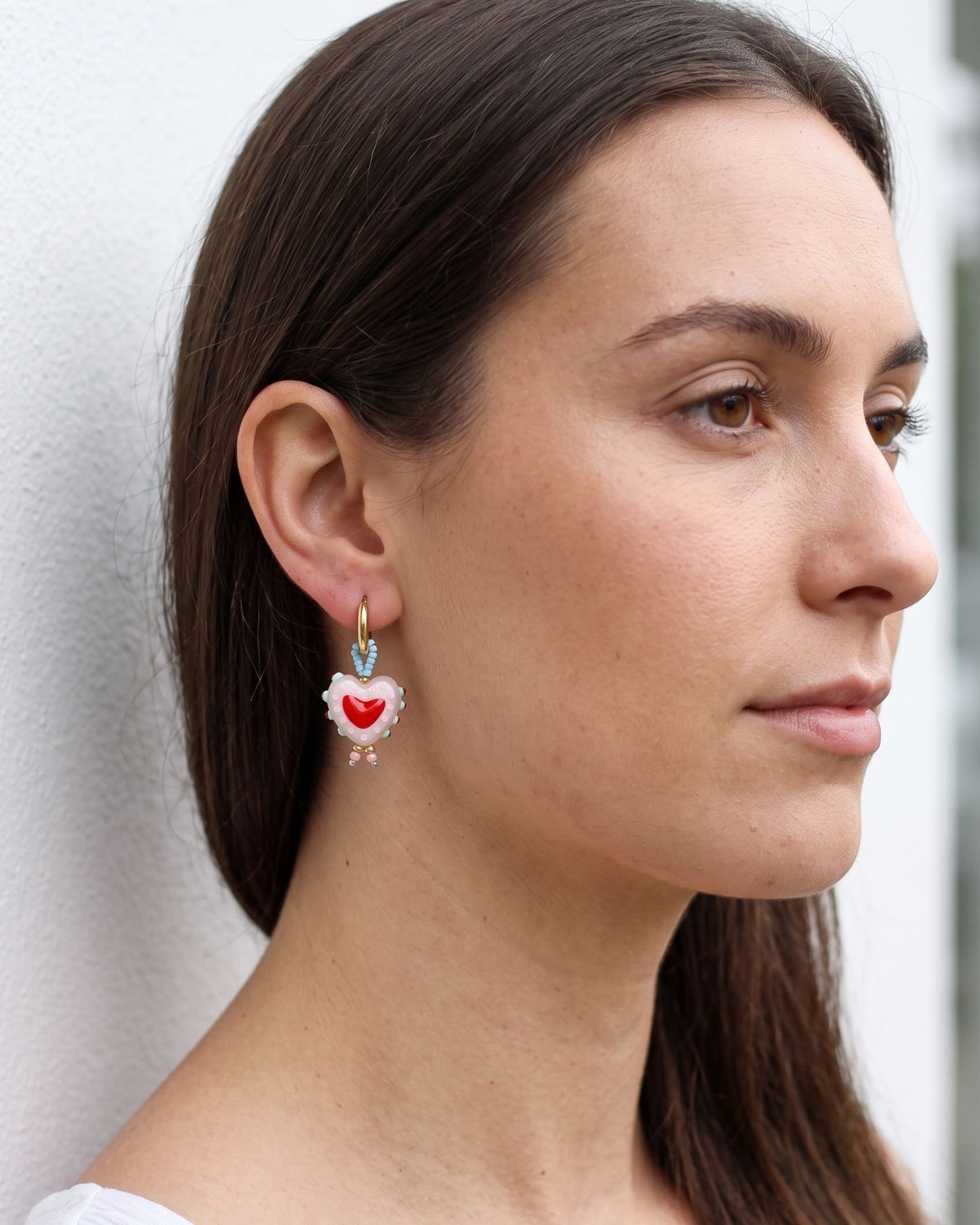 Close up profile of a woman wearing small gold heart earrings with pink beads.