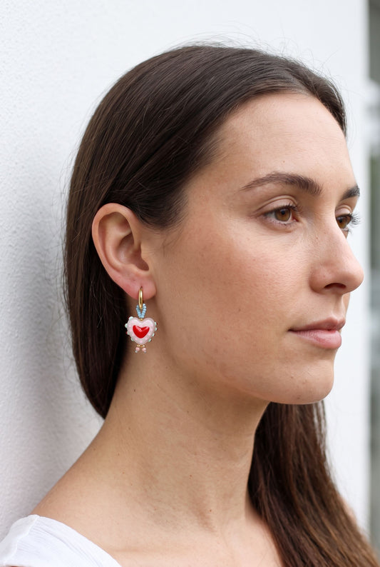 Close up profile of a woman wearing small gold heart earrings with pink beads.