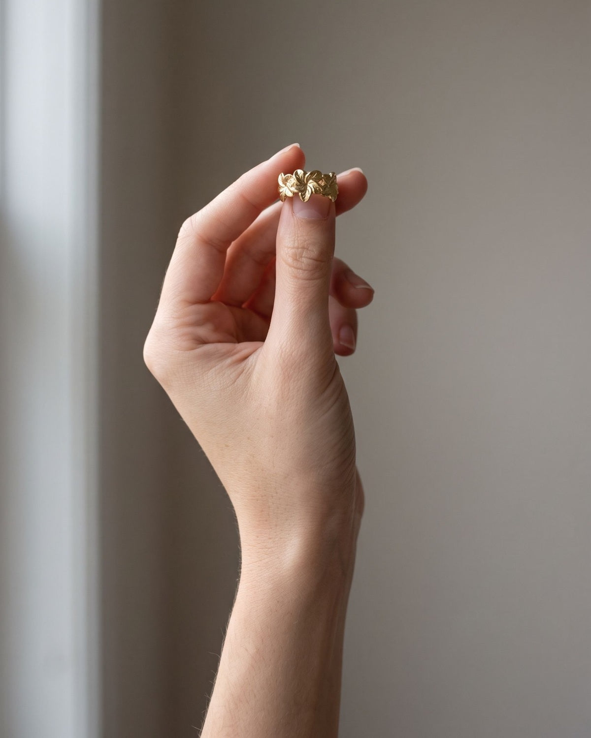 Slender hand wearing a subtle hibiscus-inspired stainless steel ring on an index finger.