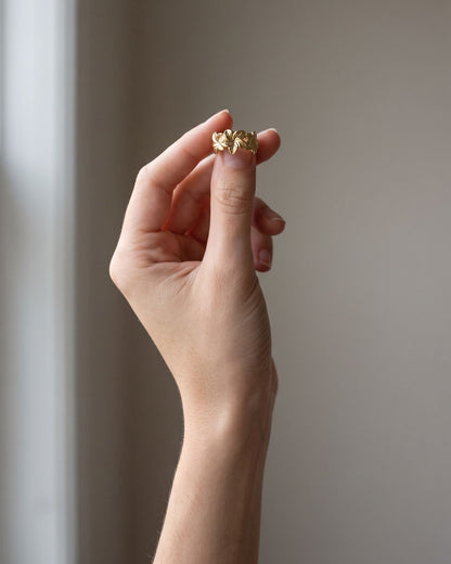 Slender hand wearing a subtle hibiscus-inspired stainless steel ring on an index finger.
