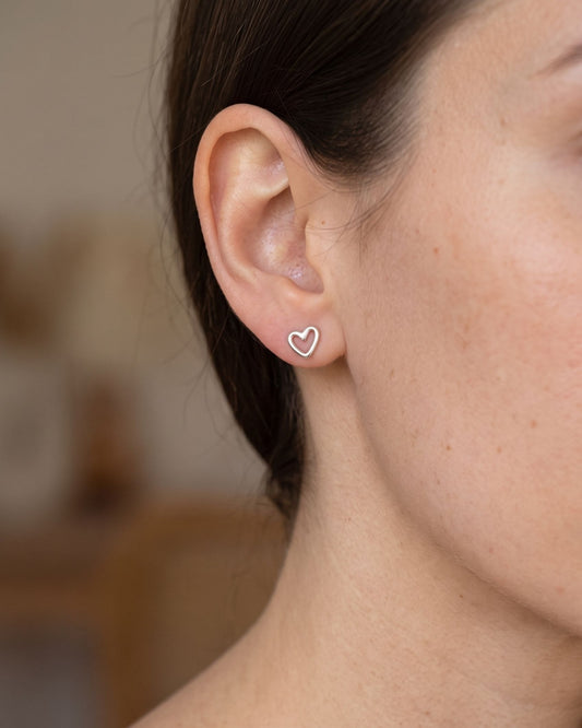 A close-up side profile of a person wearing a small delicate heart-shaped stud earring.