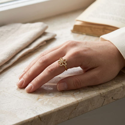 Female hand wearing the floral garden glitz ring on her finger, resting on a rustic marble surface with soft natural lighting highlighting the jewelry's femininity.