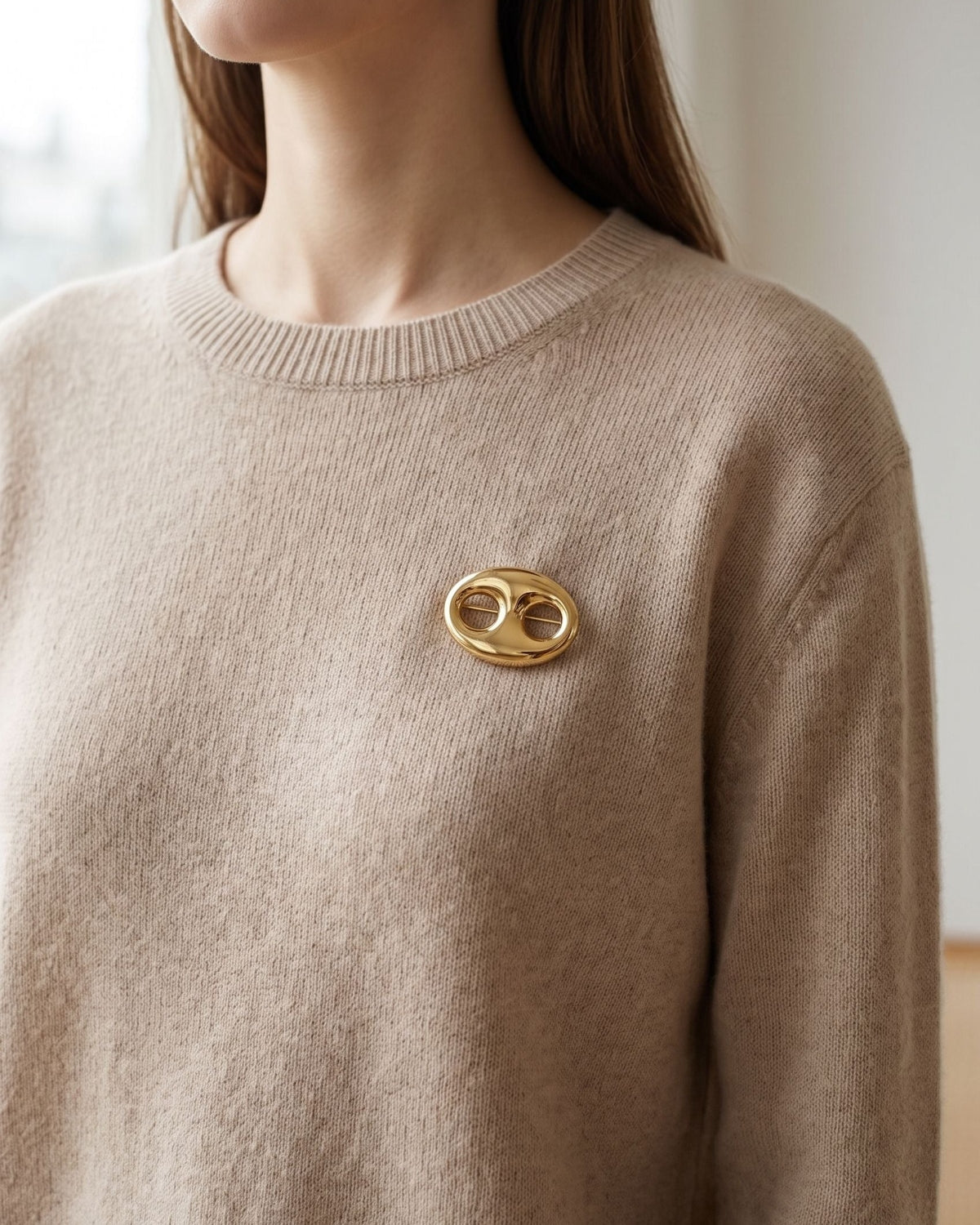 Gold irregular brooch pinned to a neutral beige cashmere sweater on a model.