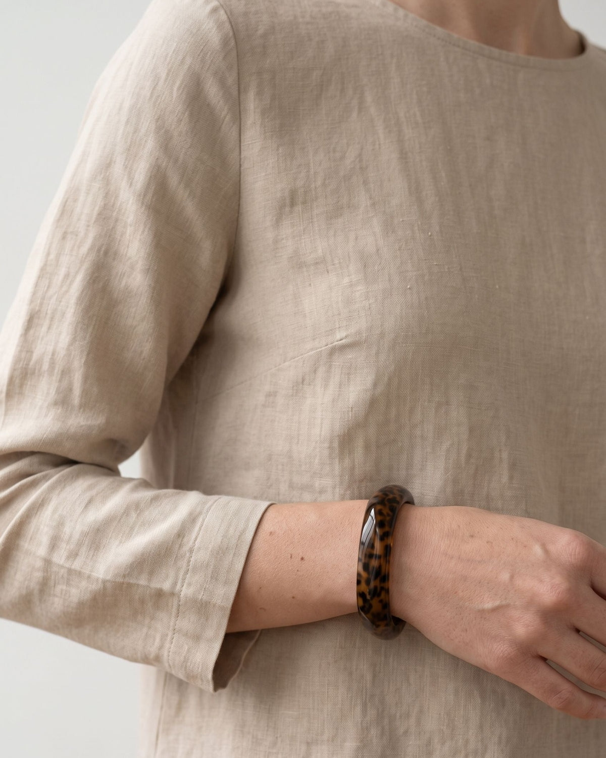 A petite brown leopard print resin bangle worn on the wrist with a neutral linen long-sleeve top.