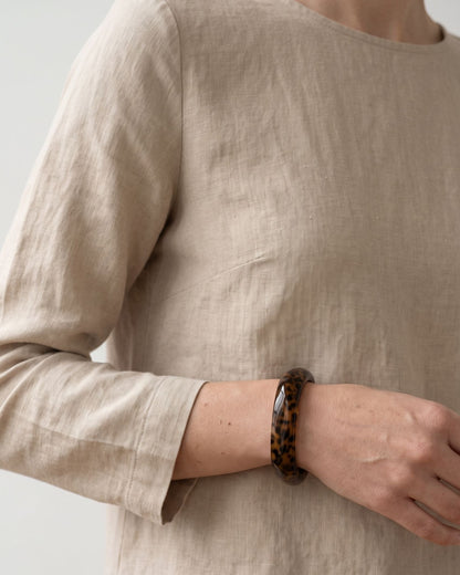 A petite brown leopard print resin bangle worn on the wrist with a neutral linen long-sleeve top.