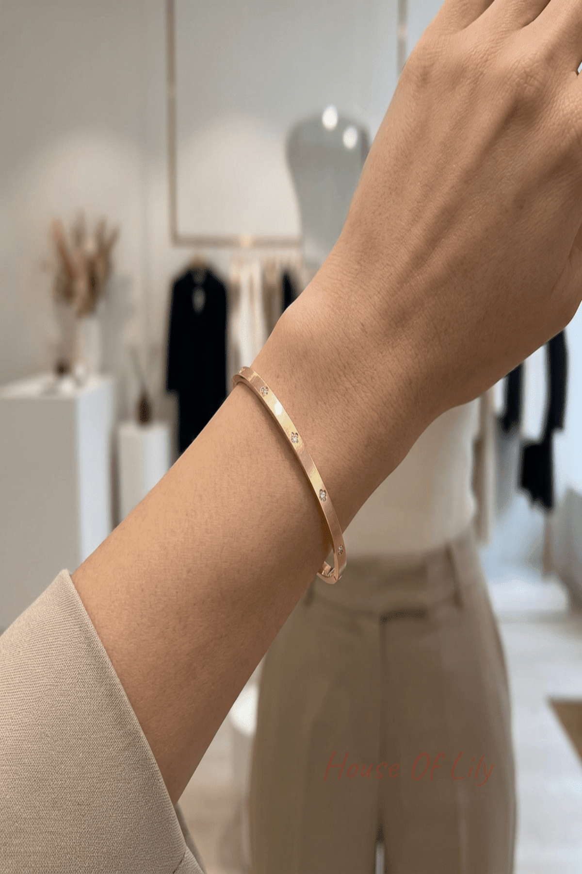 Stylish woman in a modern boutique wearing a slim gold bangle on her wrist, showcasing minimalist jewelry in a chic setting.