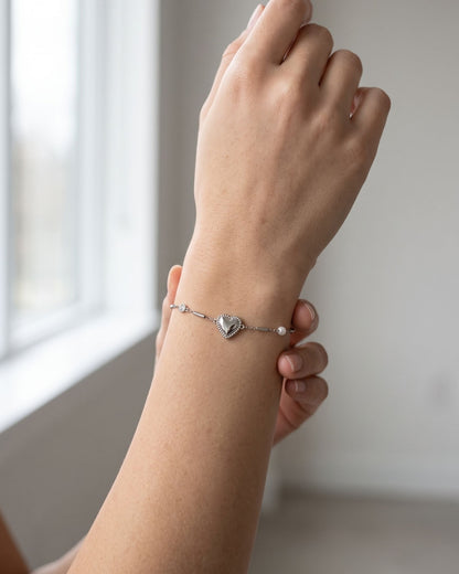 Minimalist stainless steel heart charm bracelet worn on a wrist in soft natural window light.