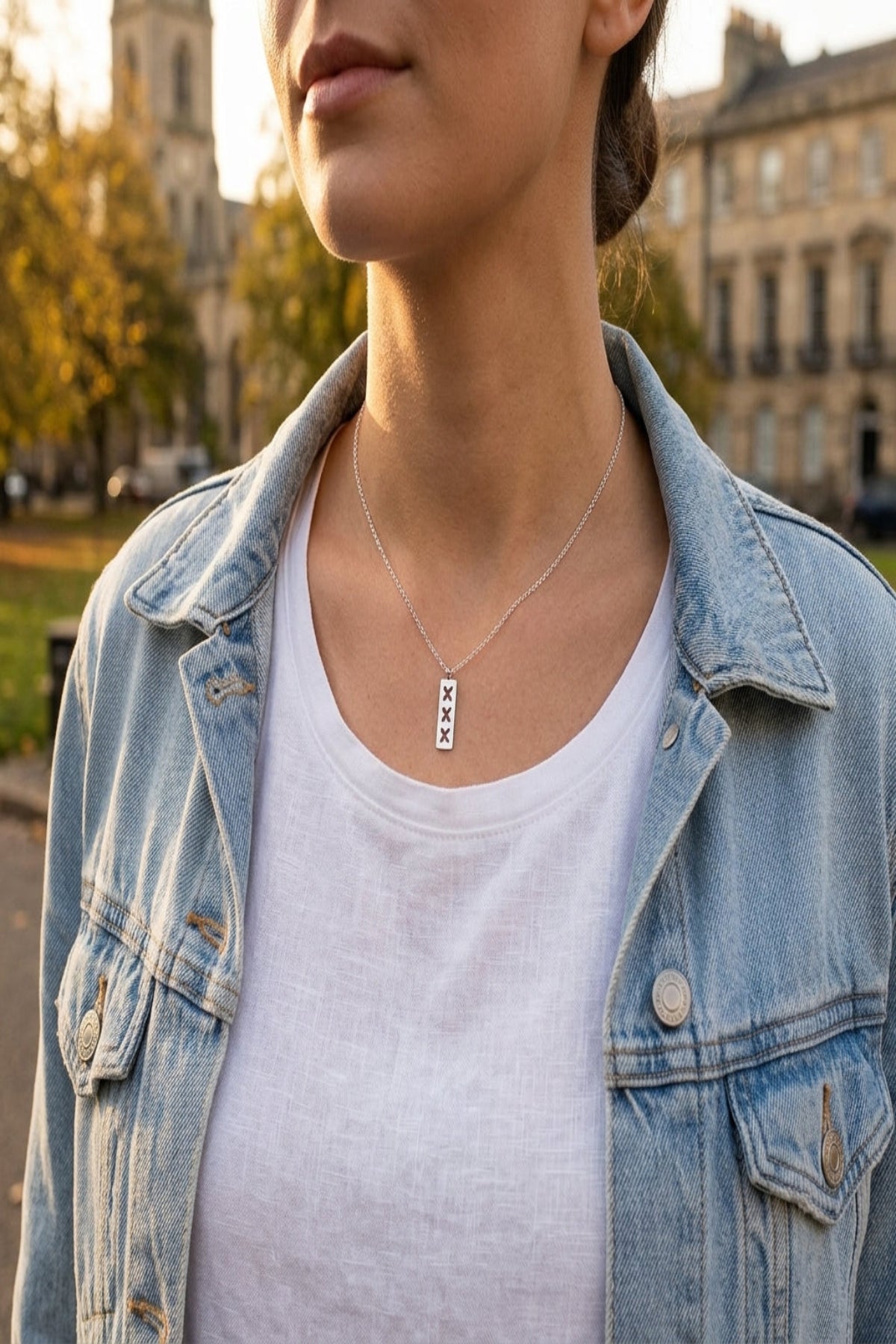 Stylish woman outdoors during golden hour wearing adjustable silver-tone triple X pendant necklace at clavicle level.