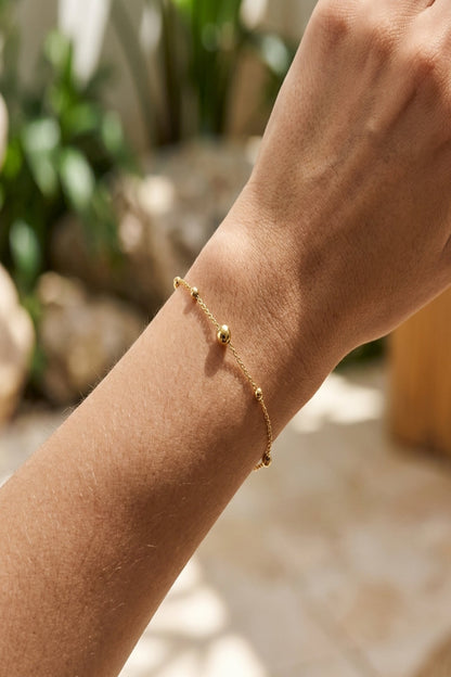 Full-body shot of a woman wearing the minimalist stainless steel bracelet in a natural, softly lit environment.