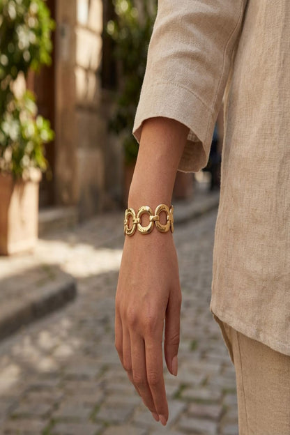 Model wearing a petite oval alloy bracelet outdoors in sunlight, showcasing its slim profile and casual, stylish appeal in an urban environment.